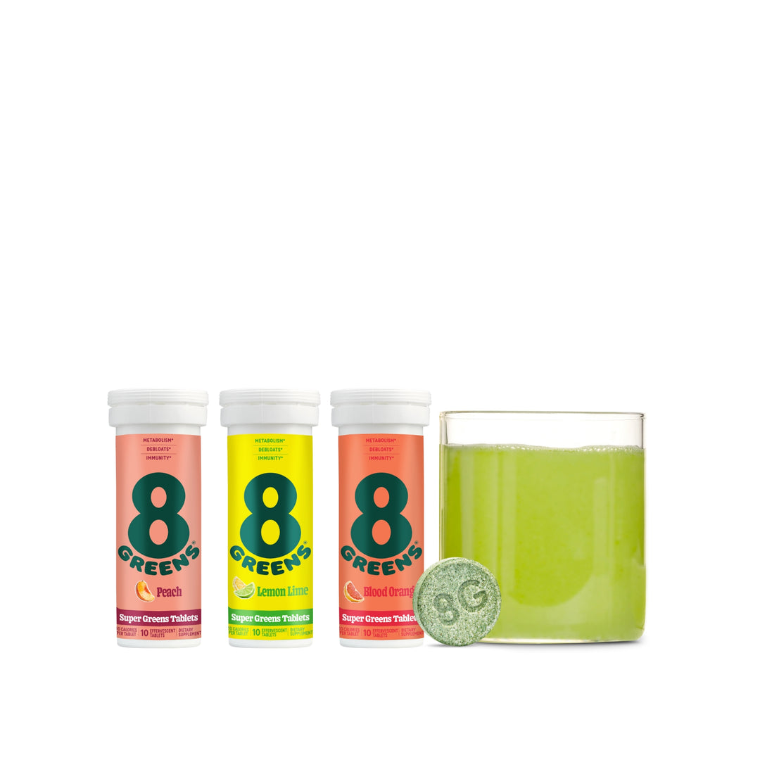 8Greens tablet packages in peach, lemon lime, and blood orange, next to prepared green drink in glass